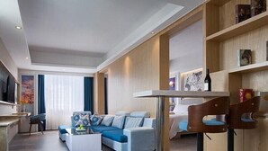 A modern living room with a sofa, a coffee table, and a dining area with bar stools. - Kyriad Marvelous Hotel (Dongguan)