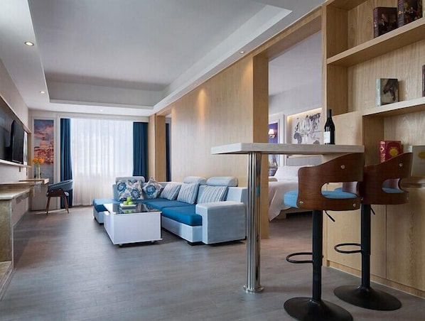 A modern living room with a sofa, a coffee table, and a dining area with bar stools. - Kyriad Marvelous Hotel (Dongguan)
