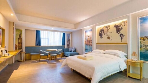 A hotel room with a large bed, a seating area with a table and chairs, a world map on the wall, and a view of the sea through the window. - Kyriad Marvelous Hotel (Dongguan)