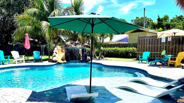 Een zwembad met een waterval, omringd door ligbedden en parasols.