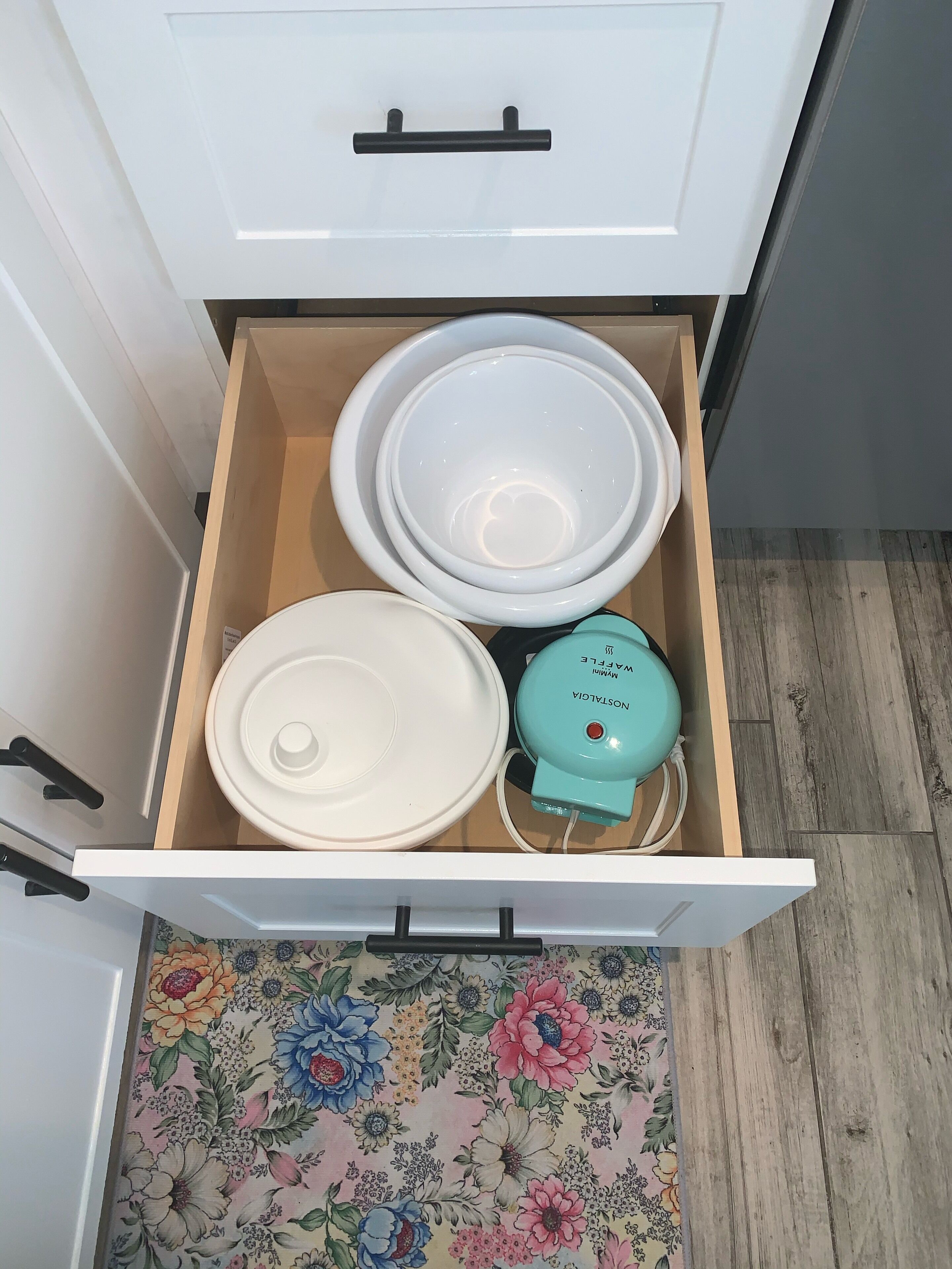 A kitchen drawer with white plates, a white bowl, and a teal water filter.