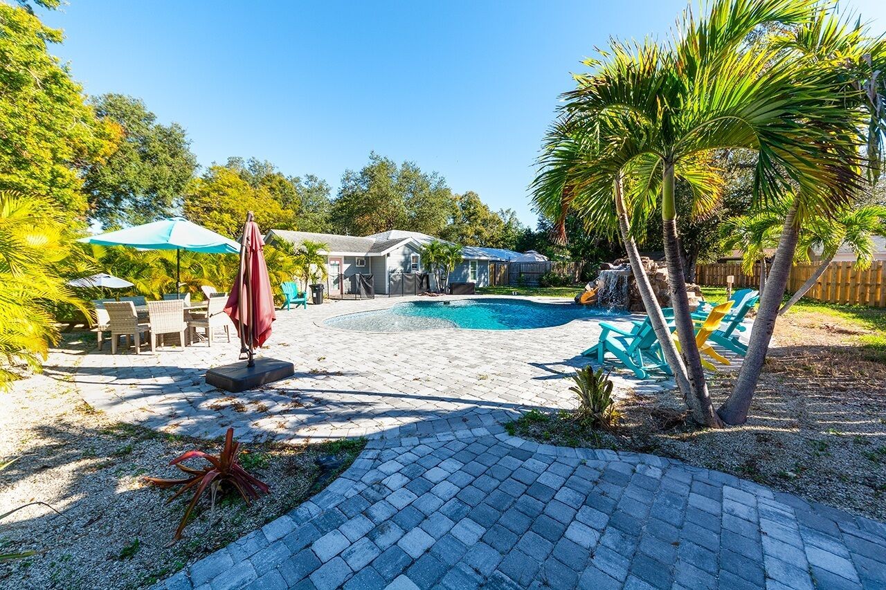 A backyard with a swimming pool, patio furniture, and palm trees.