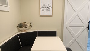 Een zithoek met hoekbank, een witte tafel en zwarte gestoffeerde bankjes, een lijst met een citaat aan de muur en een visdecoratie.