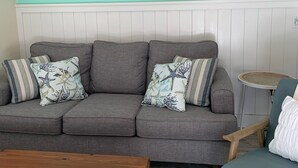 Een woonkamer met een grijze bank, twee decoratieve zeesterren aan de muur en een houten salontafel.