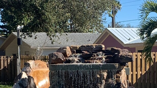 A swimming pool with a waterfall feature, surrounded by a wooden fence and a palm tree. - WATER SLIDE & POOL ** Sugarcane Hideaway** (Bradenton)