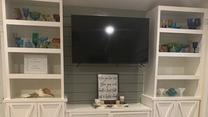 A living room with a TV mounted on the wall, surrounded by white shelving units with decorative items. - WATER SLIDE & POOL ** Sugarcane Hideaway** (Bradenton)