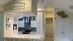 A modern kitchen with white cabinetry, a central island with bar stools, and decorative wall art. - WATER SLIDE & POOL ** Sugarcane Hideaway** (Bradenton)