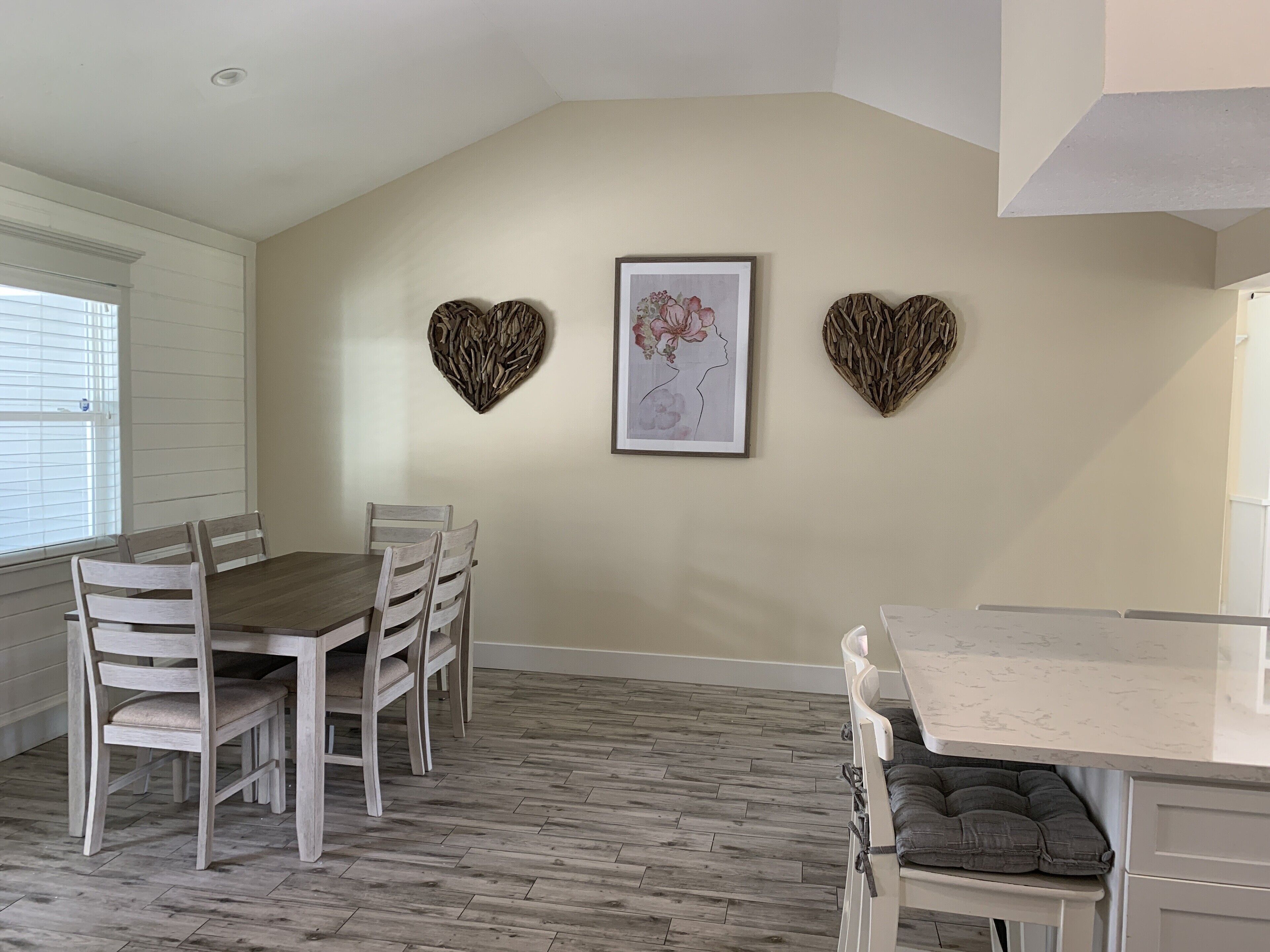 A dining area with a wooden table and chairs, a white cabinet, and decorative heart-shaped wall art.