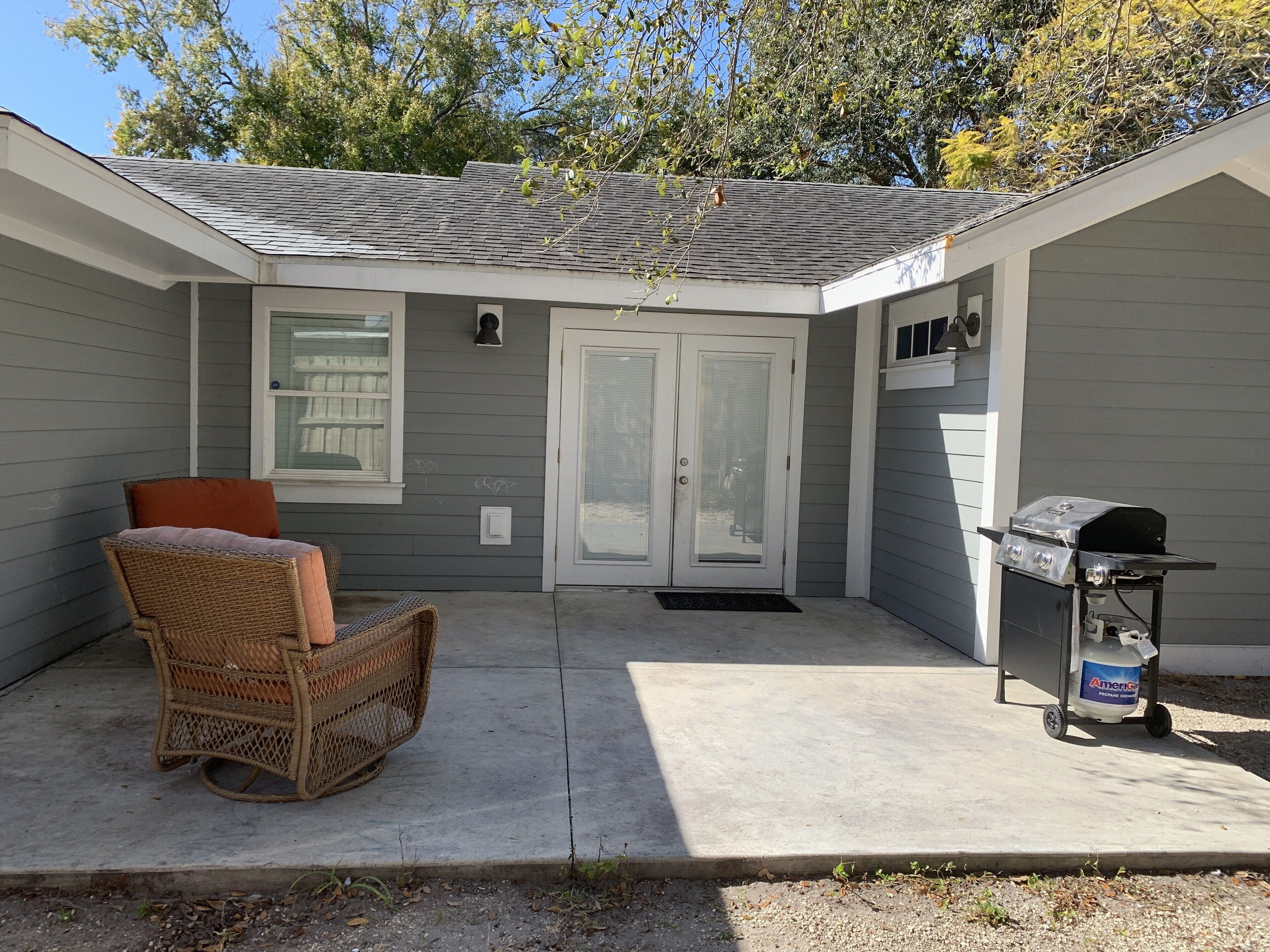 A covered patio with a wicker chair, a grill, and a door with a window.