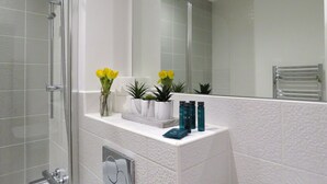 A modern bathroom with a glass shower enclosure, a white vanity with toiletries, and a mirror reflecting the space.