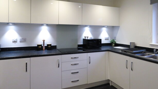 A modern kitchen with white cabinets, black countertops, and under-cabinet lighting.
