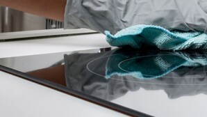 A hand wearing a glove cleaning a reflective surface, likely a mirror or glass.