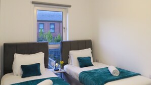 A hotel room with two beds, a window with a view of a brick building, and a hanging light fixture.