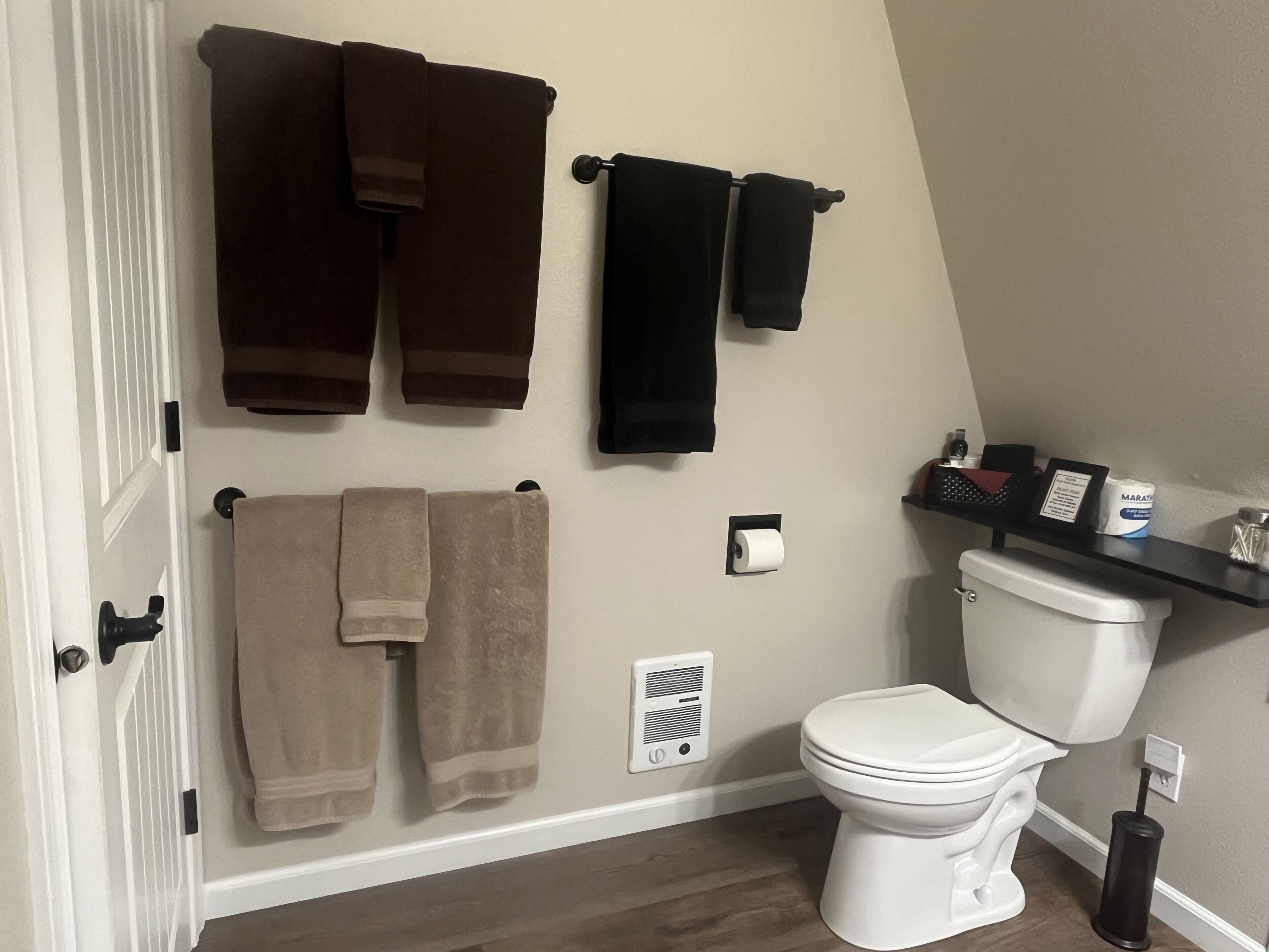 A bathroom with a toilet, towel racks, a showerhead, and a toilet paper holder.