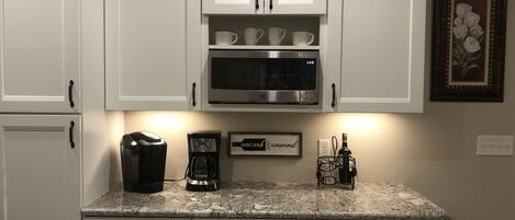 Une cuisine avec des meubles blancs, un four à micro-ondes, une machine à café et un panneau décoratif encadré posé sur le plan de travail.