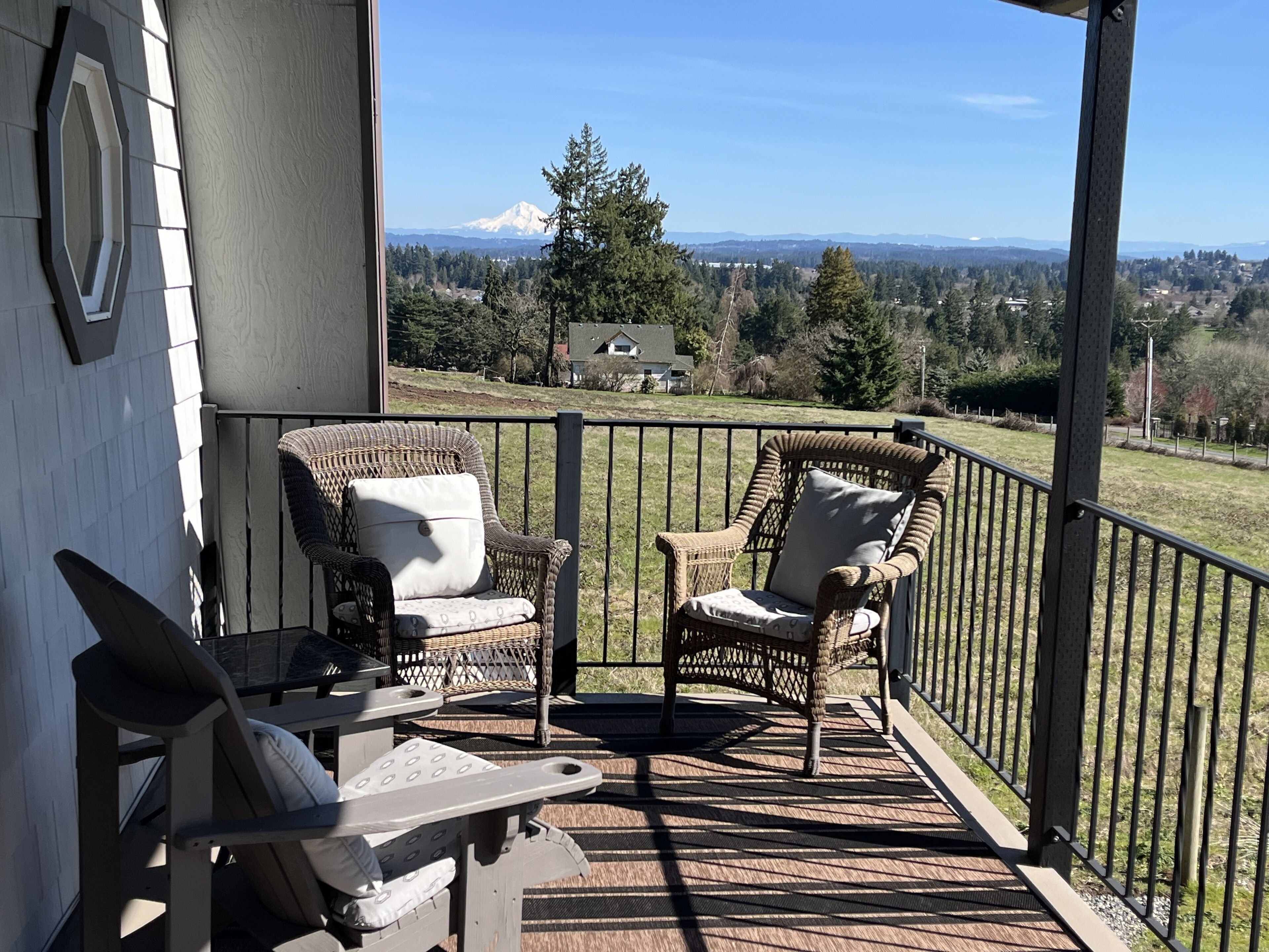 A covered outdoor seating area with wicker chairs and a table, overlooking a scenic landscape with a mountain in the distance.