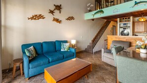 A living room with a blue sofa, a wooden coffee table, and a staircase leading to an upper level. - Beautiful, Family Friendly 2 Br 2Ba Across Street From Beach. (Kihei)