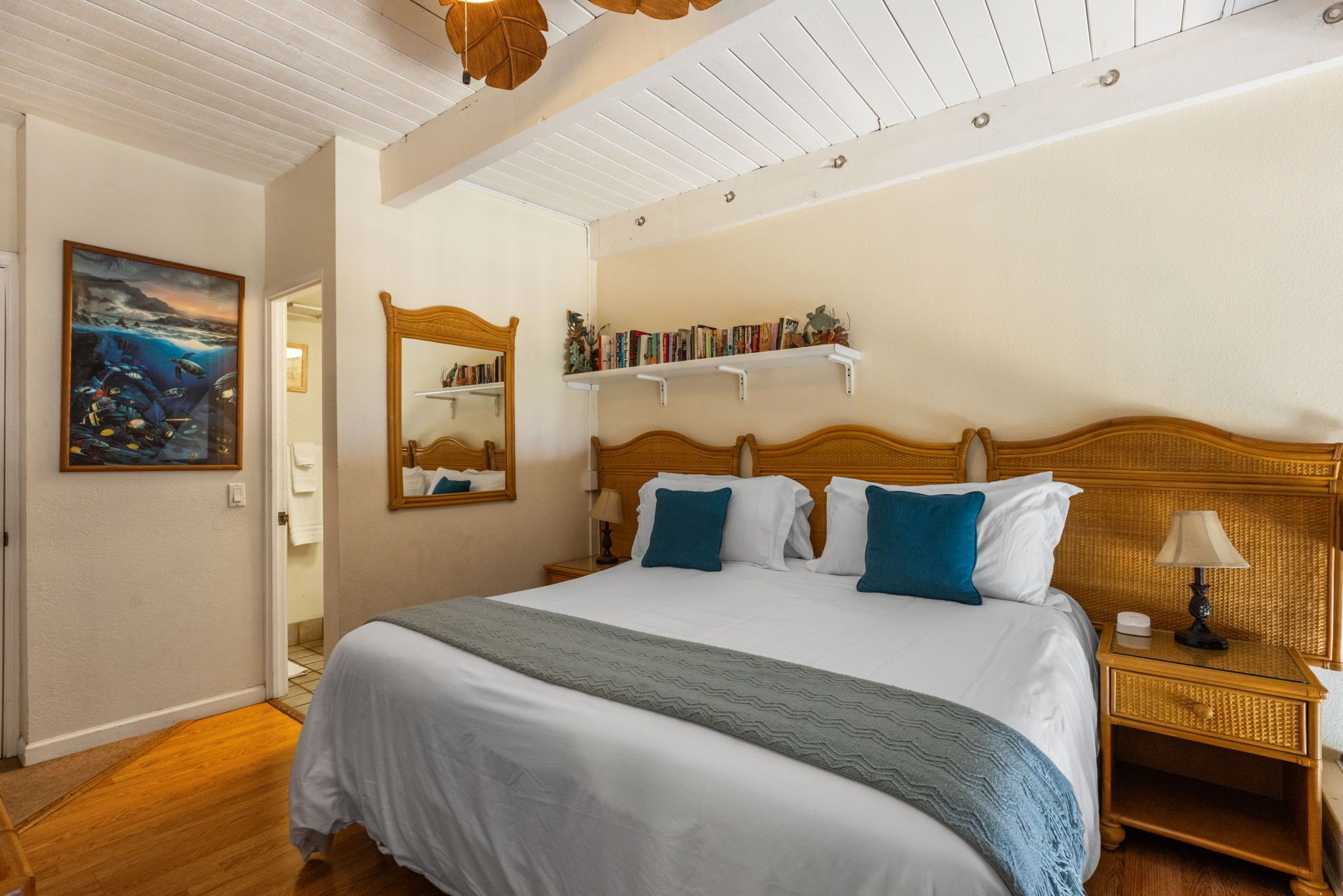 A bedroom with a large bed, a bedside table, a nightstand, a mirror, a bookshelf, and a painting on the wall.
