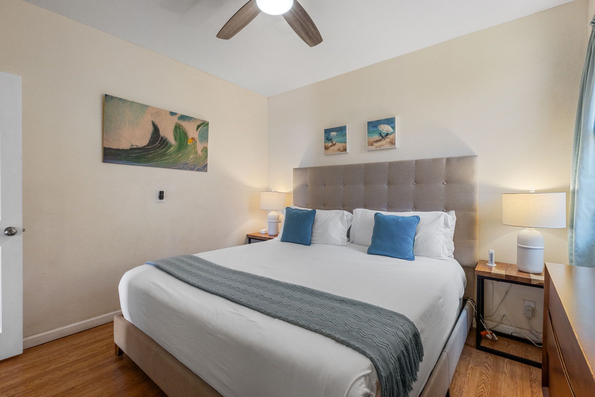 Une chambre avec un grand lit, un ventilateur de plafond et des œuvres d’art accrochées aux murs.
