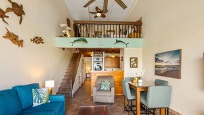 A spacious living area with a sofa, dining table, and chairs, a staircase leading to an upper level, and decorative wall art. - Beautiful, Family Friendly 2 Br 2Ba Across Street From Beach. (Kihei)