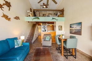 A spacious living area with a sofa, dining table, and chairs, a staircase leading to an upper level, and decorative wall art.