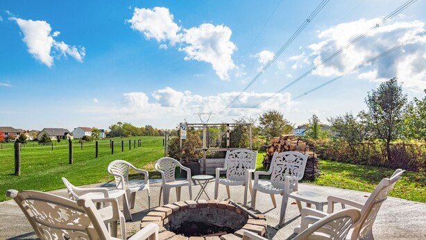 Een terras met witte stoelen en een vuurkorf, omringd door een grasveld en een heldere blauwe lucht.