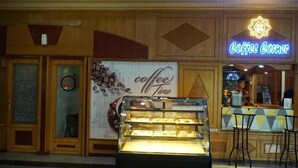 Una cafetería con un letrero de neón, una vitrina con pasteles y una barra donde trabaja un barista.