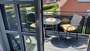 En balkon med udendørs møbler og udsigt over et boligområde, med en murstensbygning i baggrunden.