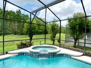 A swimming pool with a hot tub, surrounded by a glass enclosure, with a view of a grassy area and trees. - Isabellas Luxury 6BR Home Pool/Jacuzzi/Spa/GameRoom/BBQ Grill/ Mins from Disney (Davenport)