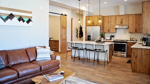 A modern kitchen with wooden cabinets, a central island with bar stools, and pendant lighting. - BRAND NEW Contemporary 2 BR near Winter Park Ski Resort on Shuttle w/priv hottub (fraser)