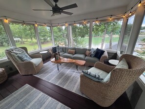 A sunroom with wicker furniture, a ceiling fan, and string lights.