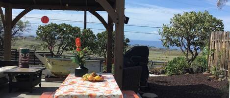 A picnic table with a 'BEACH' sign, surrounded by a wooden pergola, a tiki statue, and a boat.