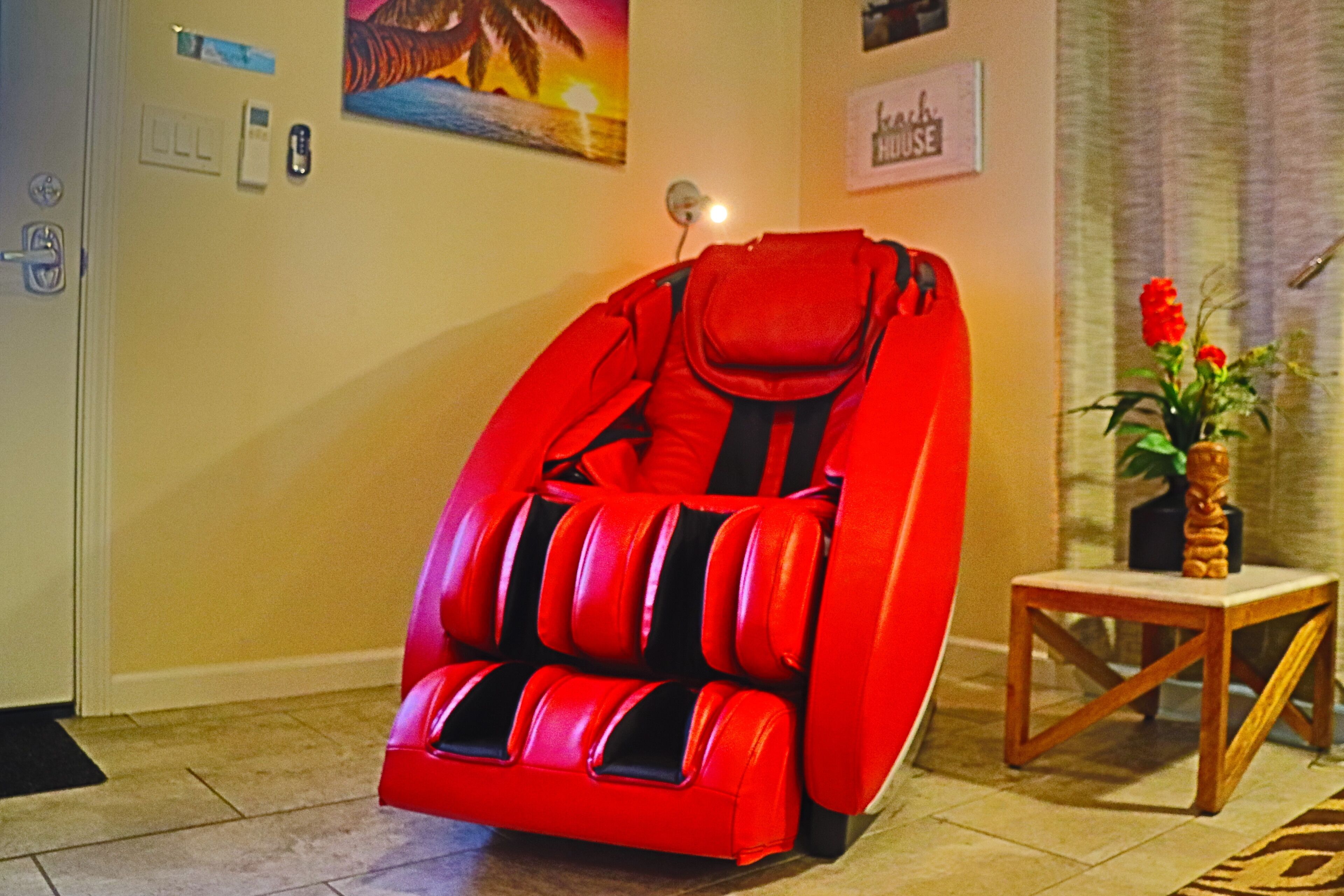 A red massage chair in a room with a small wooden table and a potted plant.