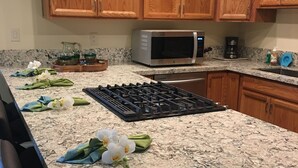 Uma cozinha com armários de madeira, bancada de granito, fogão a gás, micro-ondas e máquina de café.