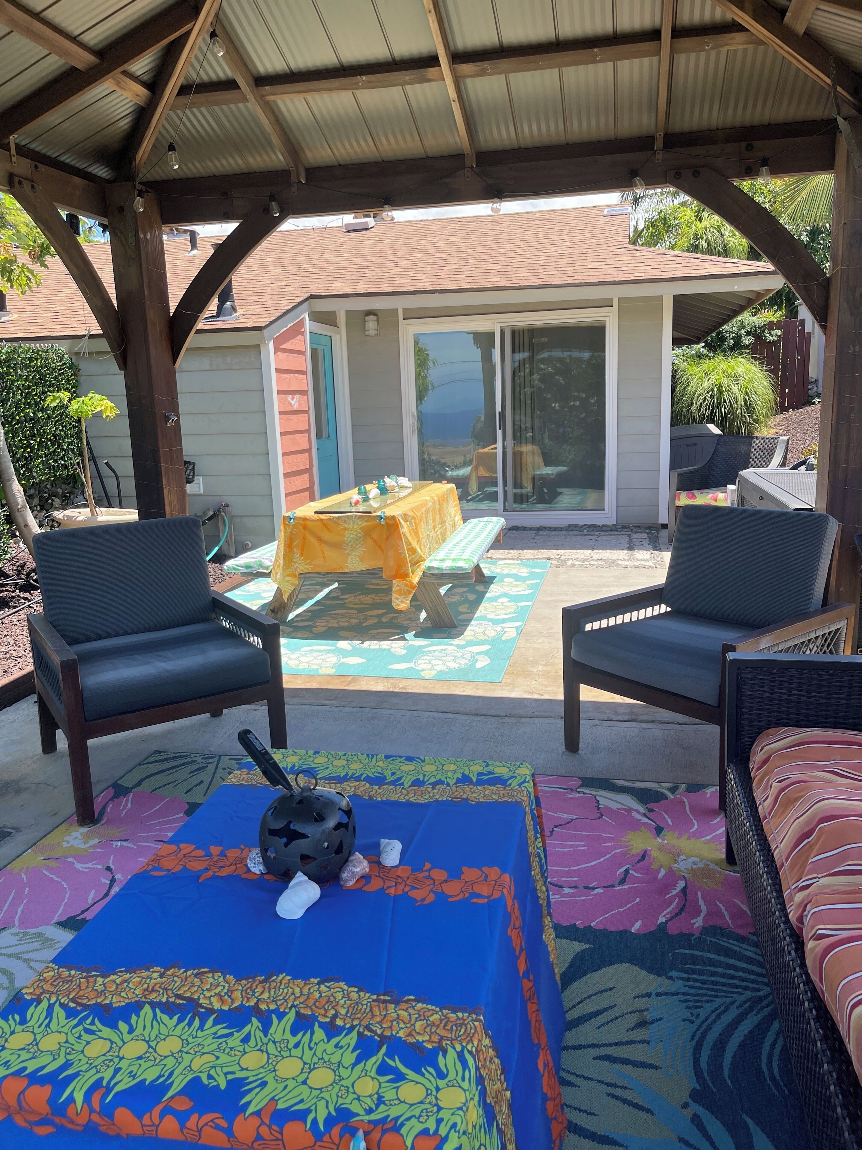 Une terrasse extérieure avec deux chaises, une table et un espace abrité offrant une vue sur une maison et un jardin.