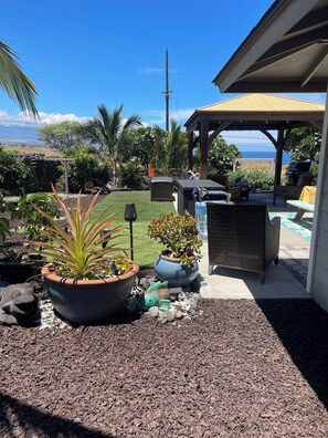 Un patio techado al aire libre con mobiliario, una parrilla y vista al océano.