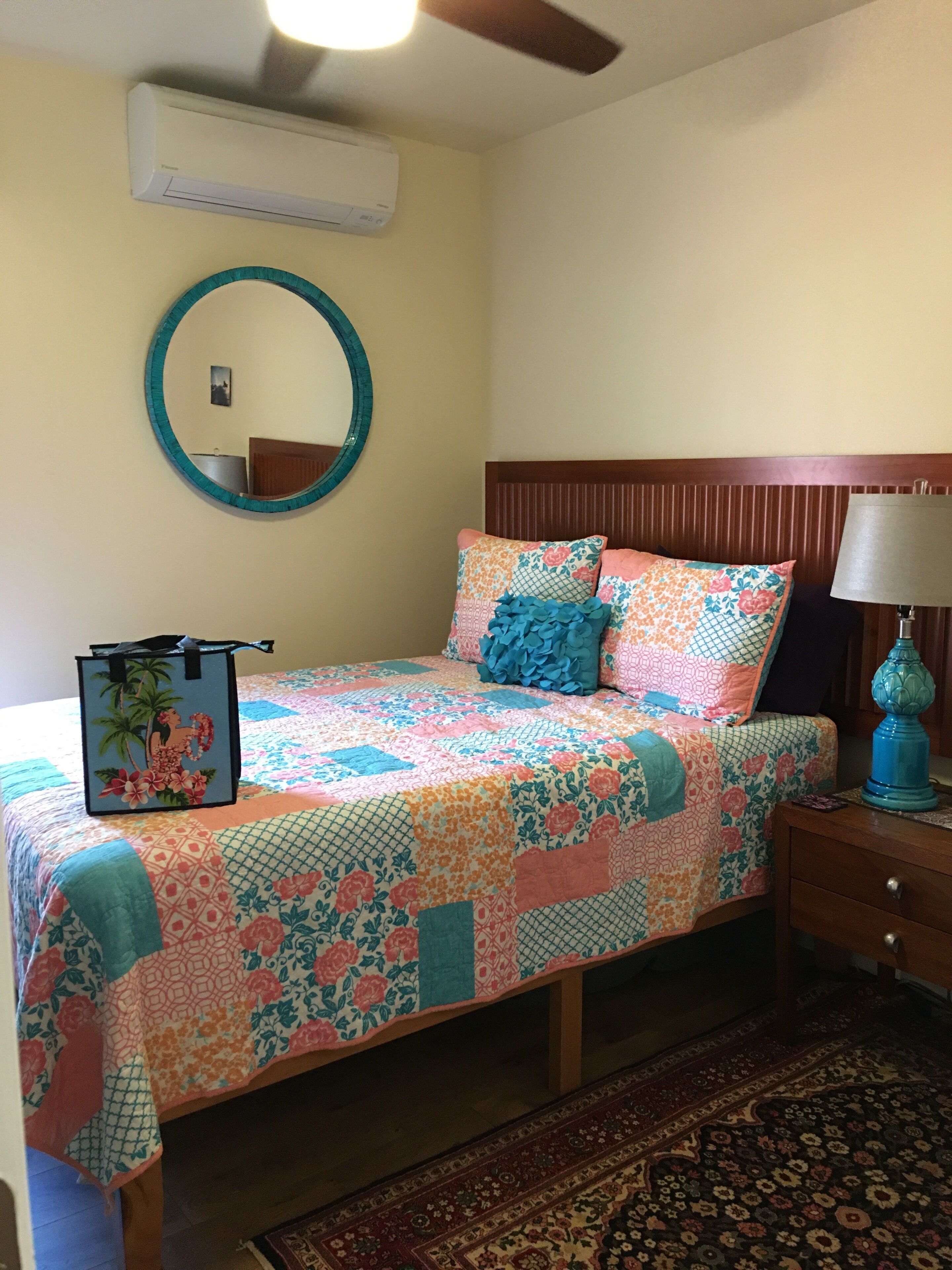 A bedroom with a bed, a nightstand, a lamp, a mirror, and an air conditioner.
