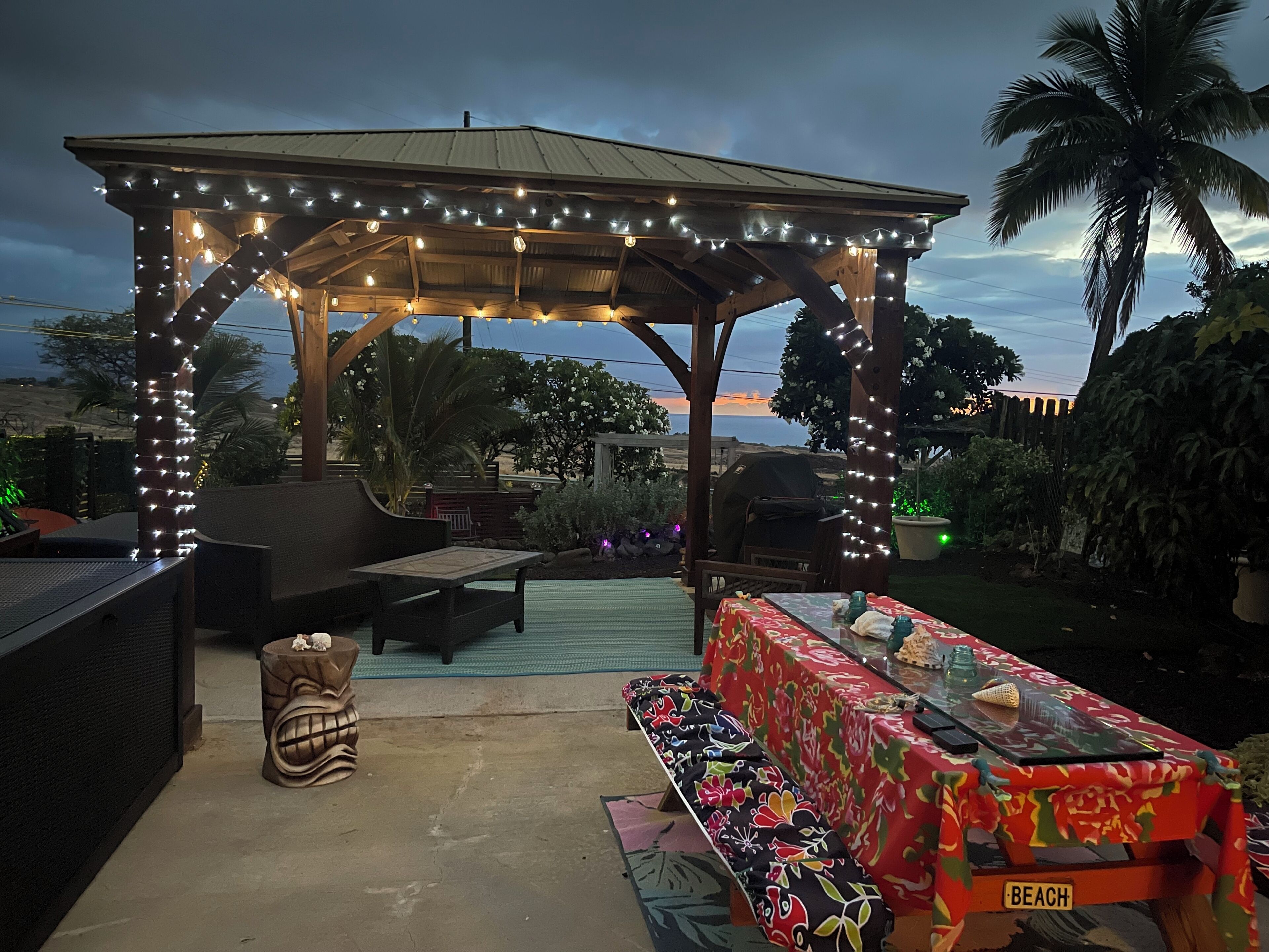 Ein Patio im Freien mit überdachter Sitzecke, einem Tisch und einem Schild mit der Aufschrift 'BEACH' sowie Lichterketten.