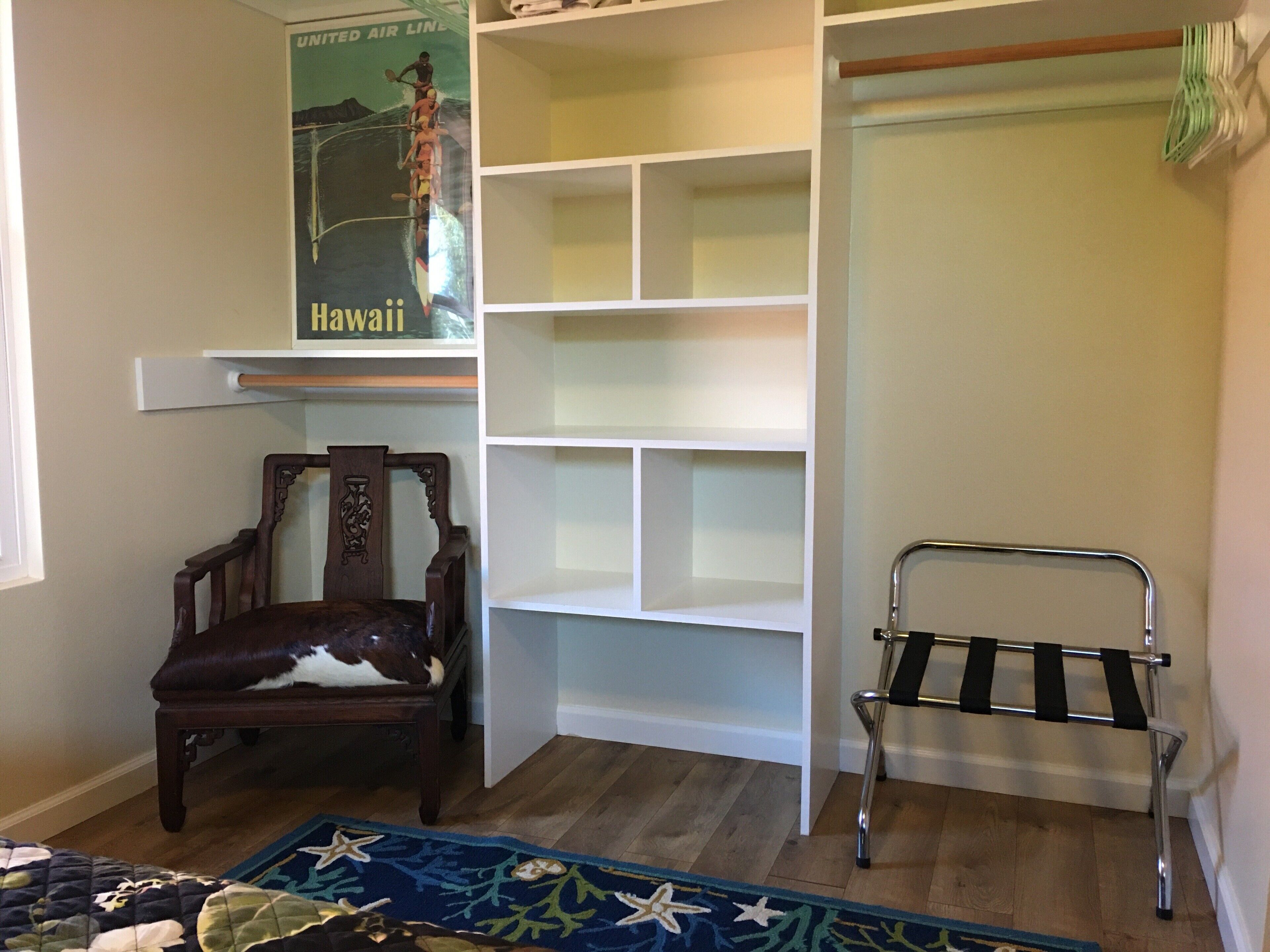 Une pièce avec une chaise en bois, un étagère en métal et un mur orné d’une affiche représentant Hawaï.