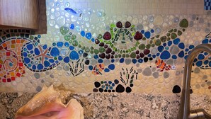 Cozinha com painel de azulejos em mosaico com tema marítimo e uma concha grande no balcão.