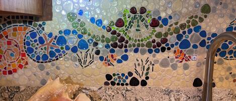 A kitchen with a mosaic backsplash featuring sea-themed tiles and a large shell on the counter.