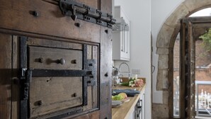 Eine rustikale Holztür mit Metallbeschlägen, eine Küchenarbeitsplatte mit verschiedenen Gegenständen und ein rundbogiger Durchgang zu einem Außenbereich.