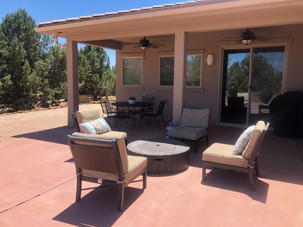 An outdoor patio area with a covered seating arrangement, including two cushioned chairs, a small round table, and a dining table with chairs. - Southern Utah getaway (Apple Valley)