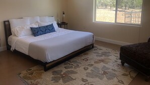 A bedroom with a bed, a nightstand, a lamp, and a view of trees through a window. - Southern Utah getaway  (Apple Valley)