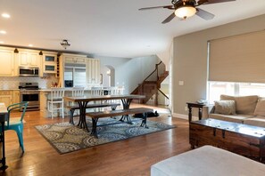 A spacious living area with a dining table, sofa, and a staircase leading to an upper floor.