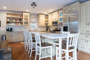 A modern kitchen with white cabinetry, a central island with bar stools, stainless steel appliances, and a patterned backsplash.