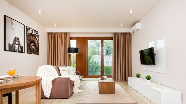 A modern living room with a sofa, coffee table, and TV. There are two paintings on the wall and a window with curtains.