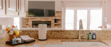 Una cocina con encimeras de granito, estufa integrada y televisor de pantalla plana sobre la estufa.