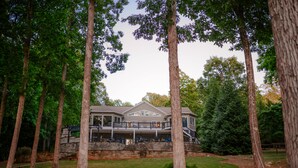 A large, modern house with a stone facade, multiple balconies, and a well-maintained lawn surrounded by tall trees. - THANKSGIVING on Lake Keowee! Sleeps 18, Dock, Fire Pits, Kayaks, Pet Friendly (Seneca)