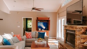 A living room with a stone fireplace, a ceiling fan, and a large window. - THANKSGIVING on Lake Keowee! Sleeps 18, Dock, Fire Pits, Kayaks, Pet Friendly (Seneca)